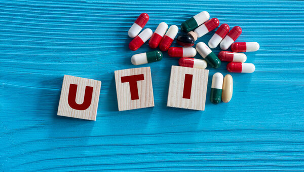 UTI (Urinary Tract Infection) - acronym on wooden cubes on a blue background with tablets. Medical concept