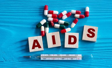 AIDS - ahşap küplerdeki kısaltma mavi arka planda, tabletler ve termometreyle. Tıbbi konsept