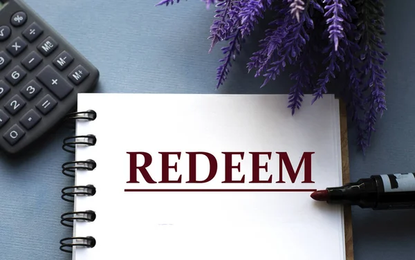 REDEEM - word are written on a notepad with a marker, calculator and lavender sprigs. Business concept