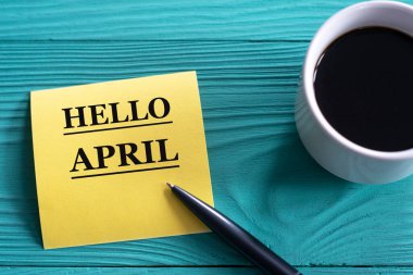 HELLO APRIL - bir fincan kahve ve bir kalem ile yeşil ahşap zemin üzerinde sarı bir kağıt parçası üzerinde kelimeler. Bilgi kavramı