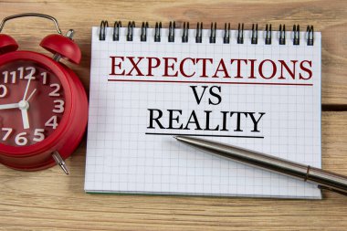 EXPECTATIONS VS REALITY - words in a notebook on a wooden background with a pen and an alarm clock. Business concept clipart