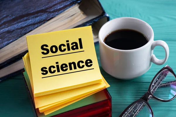 SOCIAL SCIENCE - word on yellow note sheets on a green background with a cup of coffee, glasses and folders. Business concept