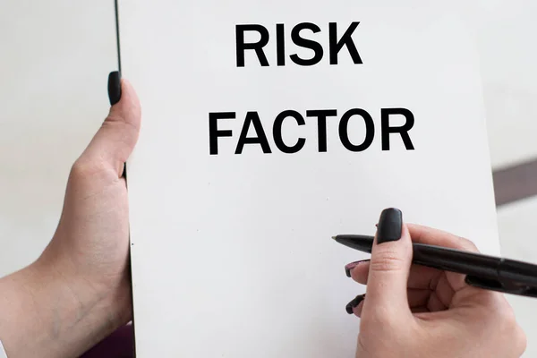 stock image words RISK FACTOR writes girl on a blank white sheet. Business concept.