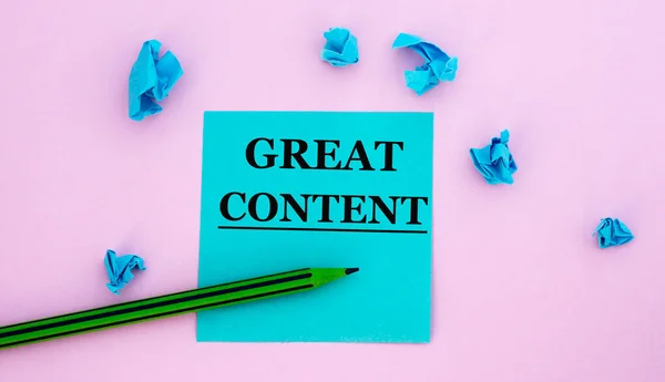 GREAT CONTENT - words on a note piece of paper on a pink background with scattered blue crumpled pieces of paper. Business concept