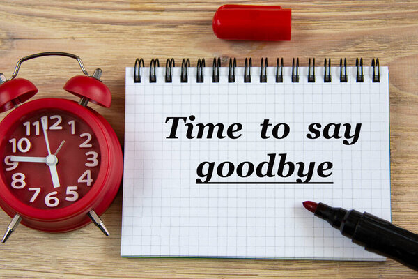 TIME TO SAY GOODBYE - слова в блокноте на деревянном фоне с будильником и маркером. Концепция бизнеса
