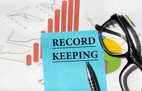 RECORD KEEPING - a word on a piece of paper for notes on the background of a graph and glasses. Business concept