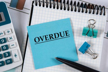 OVERDUE - bir not defteri, hesap makinesi ve kalem üzerinde mavi bir defter üzerinde kelime. İş ve finans kavramı