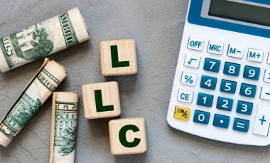 LLC (- Sınırlı Sorumluluk Şirketi) hesaplayıcı ve banknotlarla birlikte gri arkaplan üzerinde tahta küplerin kısaltması. İş konsepti