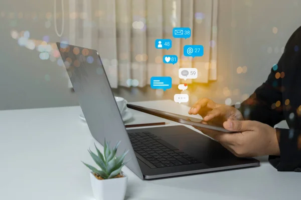 Person using a social media marketing concept on computer laptop with notification icons of like, chat, message and comment above laptop screen.