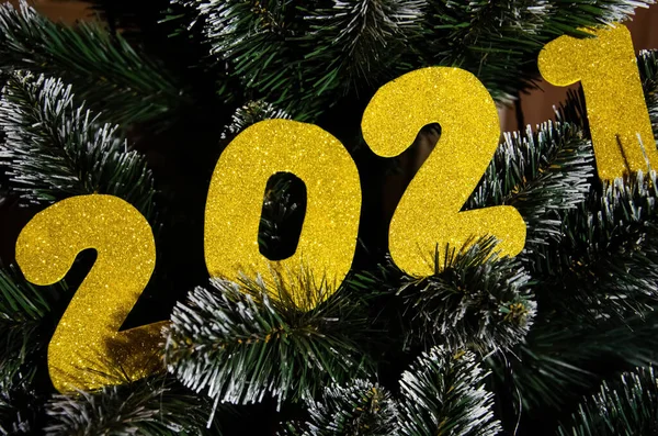 Happy New Year 2021 winter holiday greeting card. Gold shiny numbers 2021 on Christmas tree. Yellow numbers. New year concept. 2021 happy new year background with metallic golden colored numbers.