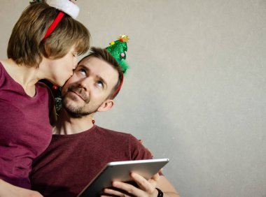 Genç çift Noel tatili boyunca eğleniyor. Beyaz kadın evde yeni yıl şapkalı bir adamı öpüyor. Birlikte mutluyuz.