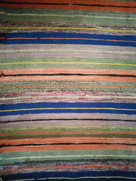 Old traditional striped carpet in Ukrainian country house. Texture of striped rough fabric. Fabric flooring in the house. Handmade carpet.