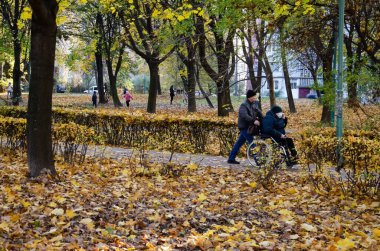Lutsk, Ukrayna - 8 Kasım 2020. Beyaz adam, sonbahar parkında telefonda konuşan koruyucu maskeli bir kadınla tekerlekli sandalye kullanıyor. İnsanlar uyku alanına park eder..