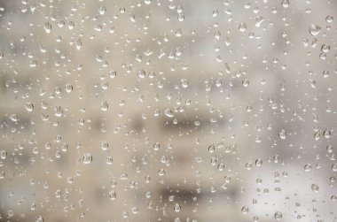 Gün boyunca penceredeki yağmur damlaları şehrin arka planına karşı. Bulanık evlerin arka planındaki cam damlalarına yakın dur. Pencerenin camına su damlaları ve bulanık binalar..