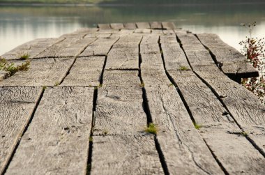 Göldeki eski ahşap iskele. Göl iskelesinde çimen olan eski tahtaların seçici odak yüzeyi. Çatallı ahşap doku. Kırsal alan. Dinlenme ve gölde balık tutma kavramı.