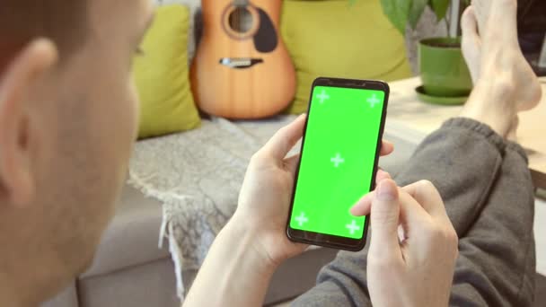 Concepto de compras en línea. Hombre se relaja en casa y en busca de información en el teléfono con pantalla verde. — Vídeo de stock