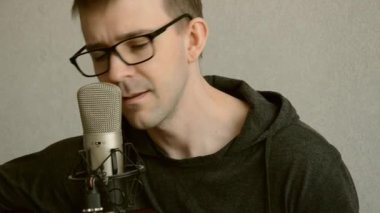Beyaz müzisyen, gitar çalıyor ve mikrofona şarkı söylüyor. Yoğunlaştırıcı mikrofonun önünde oturan bir erkek kayıt şarkısı. Müzik oluşturma kavramı.