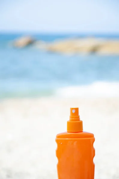 Orange bottle with sunscreen on blurred sea coast background. Suntan lotion bottles in the sand. Bottle on beach with copy space. Summer vacation concept. Protection of the skin from the sun\'s rays.