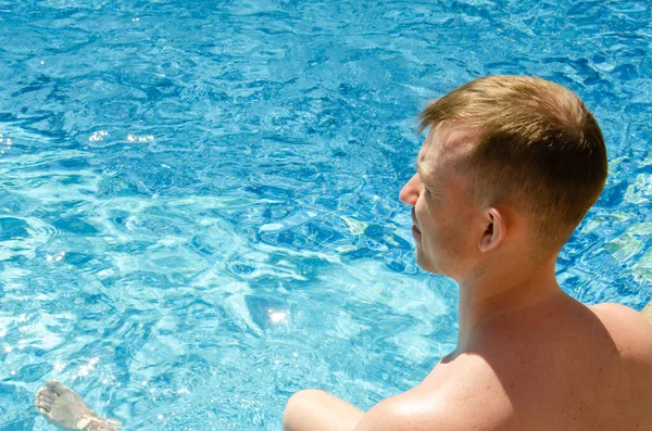 Caucasian man sitting on the pool bar with clear azure water. Adult male relaxing by the swimming pool. Summer vacation concept. Chill guy in the pool on summer day.