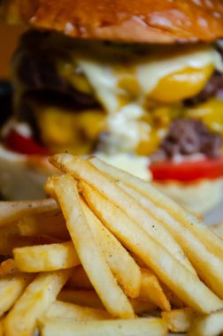 Bulanık hamburger arka planında kızarmış patates. Sağlıksız gıda konsepti. Lezzetli fast food. Kurutulmuş çörek, erimiş peynir, köfte ve sebzeli sulu hamburger..