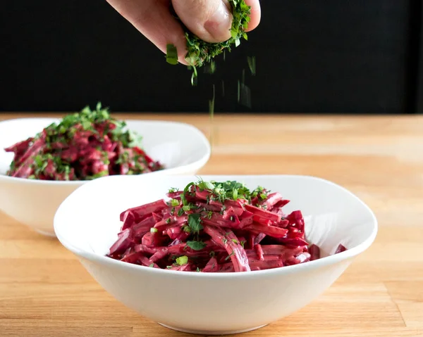 Red salad with beets in a white bowl. Sprinkle the dish with fresh herbs