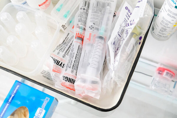 The syringes in the package are on the treatment table in the medical room. Different jars, tools and gloves nearby.