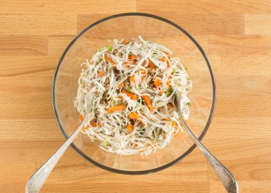 Şeffaf bir kasede konserve balıklı sebze salatası. Çatallar öne çıkıyor.