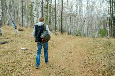 Sırt çantalı bir adam baharda ormanda yürür. Sarı solmuş yapraklar.