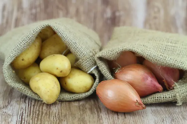 Batatas novas e chalotas em sacos de juta, close-up — Fotografia de Stock