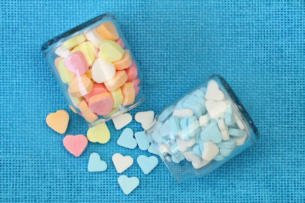 Coração de açúcar colorido em garrafas transparentes no fundo azul — Fotografia de Stock