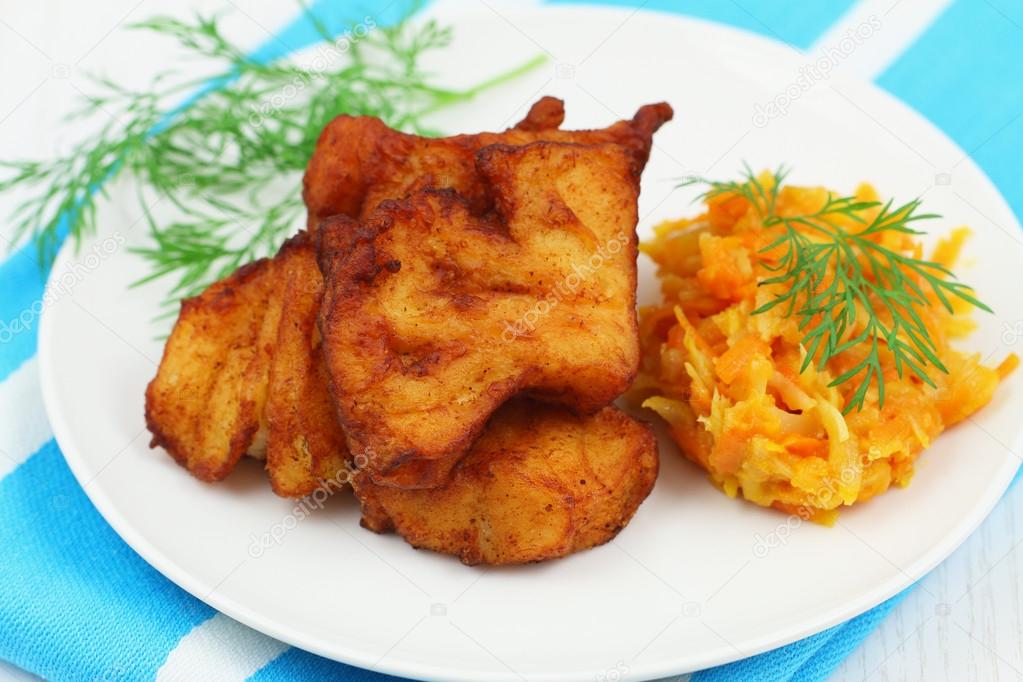 Fried cod pieces with stir fried vegetables on white plate