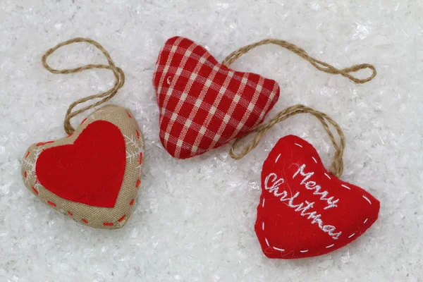 Frohe Weihnachtskarte mit drei roten Herzen, auf verschneiter Oberfläche — Stockfoto