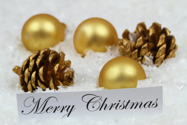 Feliz cartão de Natal com bugigangas douradas, cones de pinho na superfície nevada — Fotografia de Stock