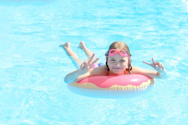 Şirin küçük kız şişme bir çemberin üzerinde açık havuzda yüzüyor..