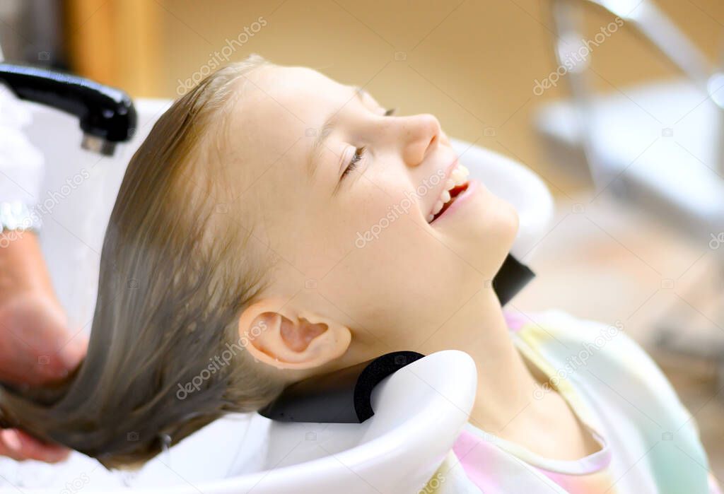 Portrait of a beautiful little girl in the hairdresser. Washing your hair with pleasure.