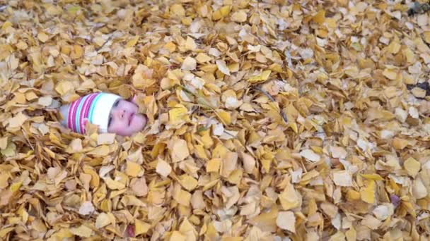 Το κορίτσι εντελώς θάφτηκε σε ένα σωρό από πεσμένα φύλλα. — Αρχείο Βίντεο