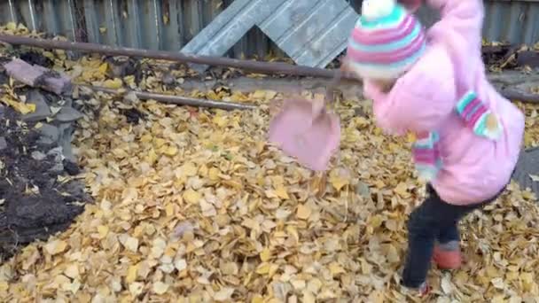 La chica lanza hojas caídas con una espátula de juguete. Otoño en el patio ruso — Vídeos de Stock