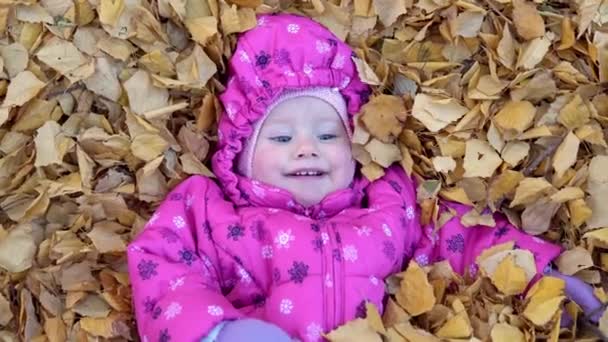 Радостное дитя, лежащее в опавших листьях — стоковое видео