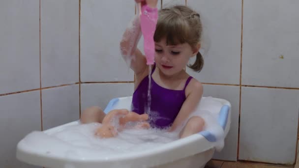 La chica se baña en un baño de bebé y baña muñecas — Vídeo de stock