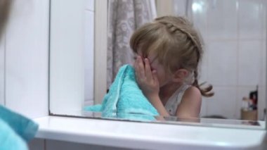 Kız aynanın önünde yüzünü havluyla siliyor.