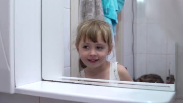Ένα κορίτσι στέκεται μπροστά από έναν καθρέφτη και σκαλίζει τη μύτη της — Αρχείο Βίντεο
