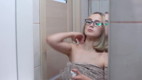 Женщина в очках перед зеркалом посыпала дезодорантом подмышки — стоковое видео