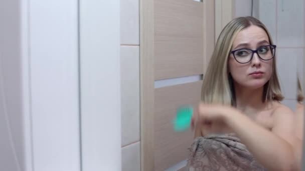 Woman with glasses in front of a mirror combing her hair — Stock Video