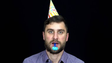 Parti şapkalı mutlu doğum günü adamı siyah arka planda parti kornası çalıyor.