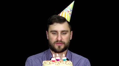 Doğum günü şapkalı adam pastanın üzerindeki mumları üflüyor.