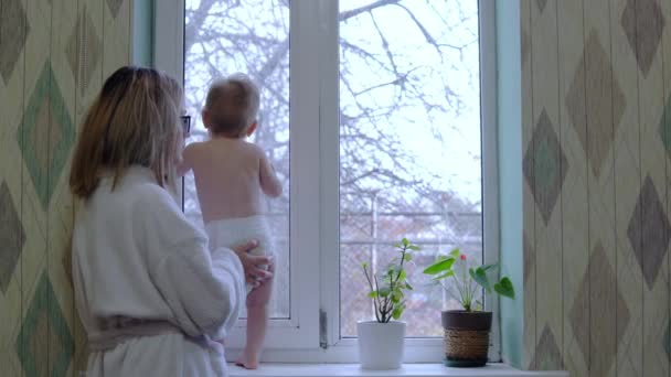 Desheveled mãe em um vestido de vestir fica com uma criança na frente da janela — Vídeo de Stock