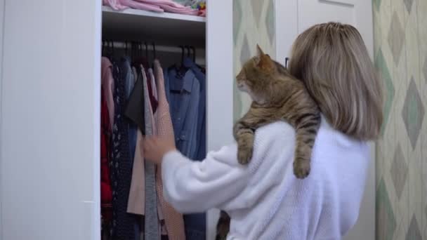 En kvinna med katt i famnen öppnar en garderob och väljer vad hon ska ha på sig. — Stockvideo