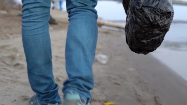 En volontär går längs stranden och samlar skräp i en påse närbild. Miljöföroreningar — Stockvideo