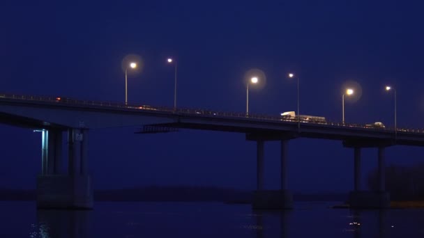 Russische brug over de rivier. De nachtbrug gloeit van lantaarns en reflecteert de schittering op het water — Stockvideo