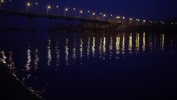 Puente de la ciudad rusa a través del río. El puente nocturno brilla con linternas y refleja el resplandor en el agua — Vídeos de Stock